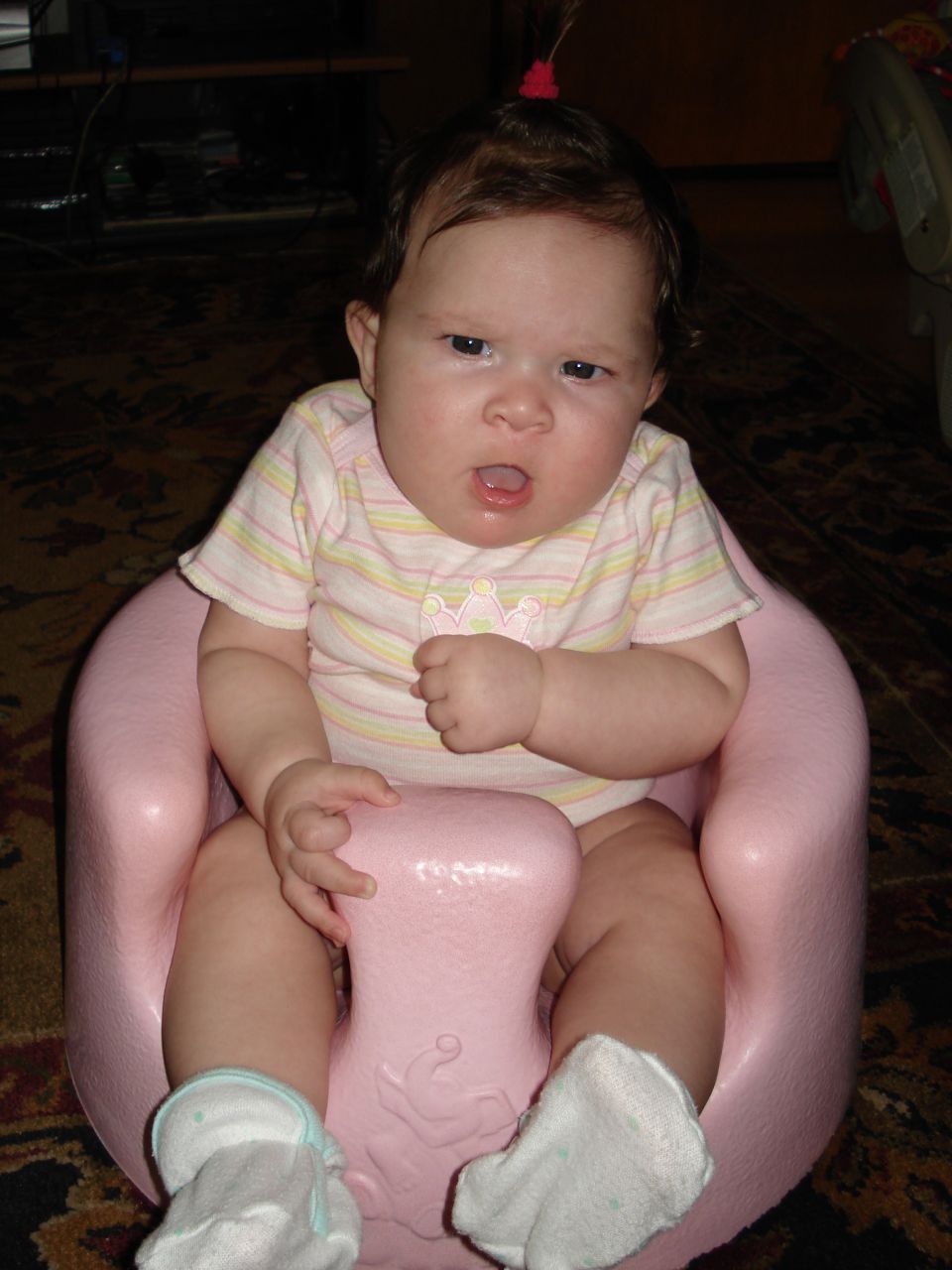 Baby in a pink seat, wearing a striped onesie and white socks