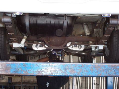 1978 Ford Mustang II - A mechanic works on the undercarriage of a vehicle, focusing on the rear suspension and dual exhaust system.