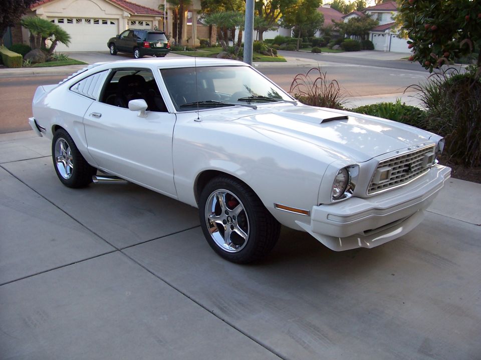 White coupe with chrome wheels and hood scoop, parked on driveway