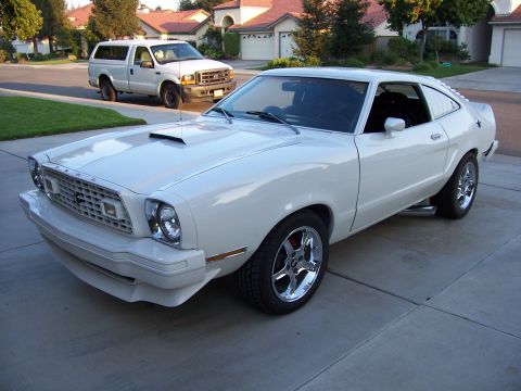 1978 Ford Mustang II - A white 1978 Ford Mustang II coupe is parked in a driveway, with a white pickup truck behind it.