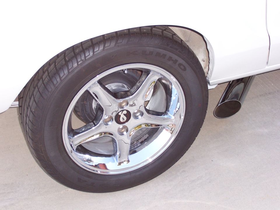 Chrome five-spoke wheel with Kumho tire and dual exhaust pipe on white vehicle