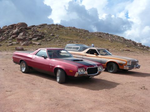 1975 Ford Ranchero - Two Ford Rancheros are parked on a dirt road with a rocky hillside and cloudy sky behind them.