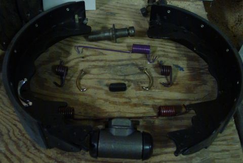 1993 Ford Bronco - A collection of brake drum components, including shoes, springs, and a wheel cylinder, laid out on a wooden surface.
