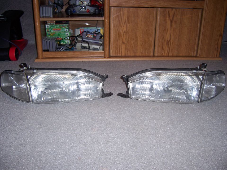 Pair of clear plastic car headlights with black mounting brackets