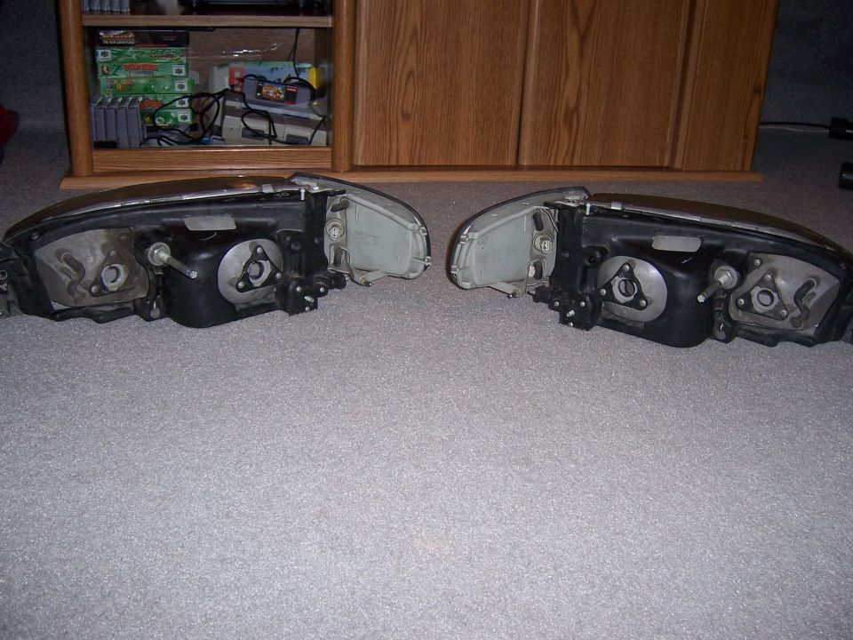 Two car headlights are lying on a carpeted floor in front of a wooden cabinet