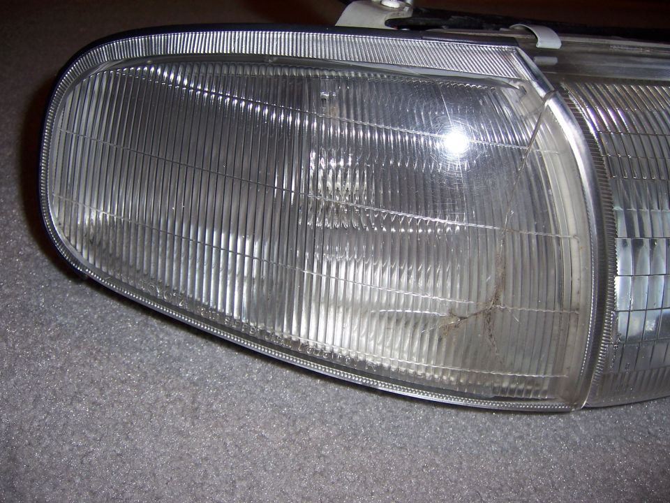 Removed composite headlight assembly with a cracked plastic lens lying on gray carpet