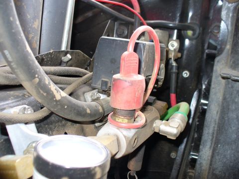 1978 Ford Bronco - This is a close-up view of an air compressor fitting with a red cap and a pressure gauge attached.