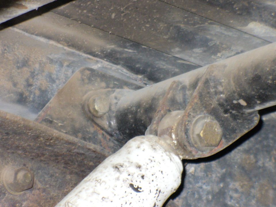 Close-up of a rusty rear shock mount with bolts and a white shock absorber