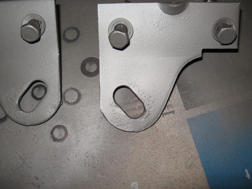 Two painted metal brackets, each secured with two bolts. Some circular marks are visible on the surface