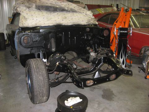 1965 Ford Galaxie - The front end of a 1965 Ford Galaxie is visible, partially covered by a sheet, with the engine removed and frame exposed.