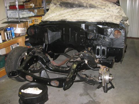 1965 Ford Galaxie - The front end of a car is disassembled, showing the frame and engine bay, with a tarp covering the upper body.