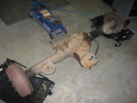 1965 Ford Galaxie - A rear axle assembly, likely from an older vehicle, sits on dollies next to a blue floor jack.