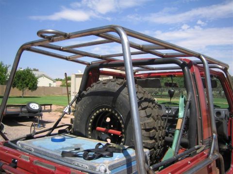 1987 Suzuki Samurai - A heavily modified off-road vehicle with a prominent external roll cage and a large spare tire is seen from the rear.