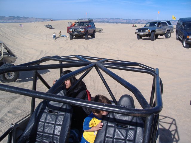 Sand dunes with multiple off-road vehicles, including a 1986 Ford Bronco, and people