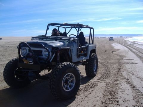 1986 Ford Bronco - A heavily modified off-road vehicle navigates a sandy terrain with another vehicle in the distance.