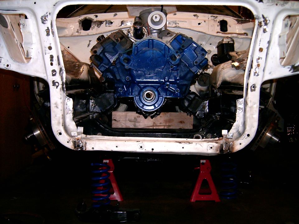 Blue Ford V8 short block mocked up in a stripped white engine bay on red jack stands