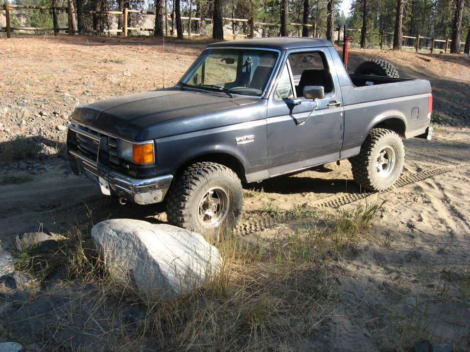 Dark blue Ford Bronco with top removed, front three-quarter view on sandy trail