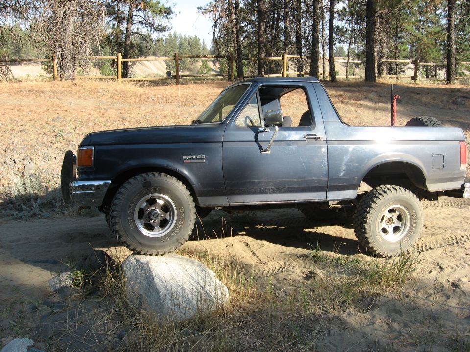 Two-tone blue and silver Ford Bronco with top removed and lifted mud tires on sandy trail