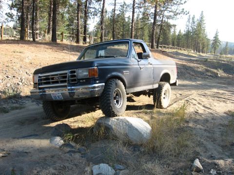 1988 Ford Bronco - This Ford Bronco is navigating an off-road trail with rocky terrain and dry grass.