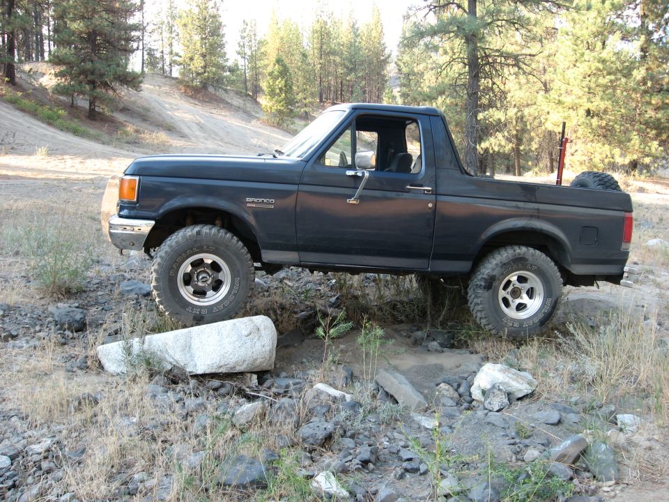 Dark blue Ford Bronco with top removed, side view, lifted on mud tires in pines
