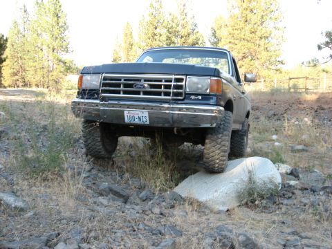 1988 Ford Bronco - Ford F-150 truck navigating a rocky trail with its front tire on a large boulder.