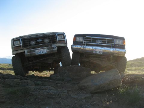 1988 Ford Bronco - Two Ford trucks navigate a rocky trail, with one vehicle's front tire lifted high.
