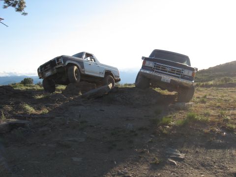 1988 Ford Bronco - Two trucks navigate a challenging off-road terrain under a clear sky.