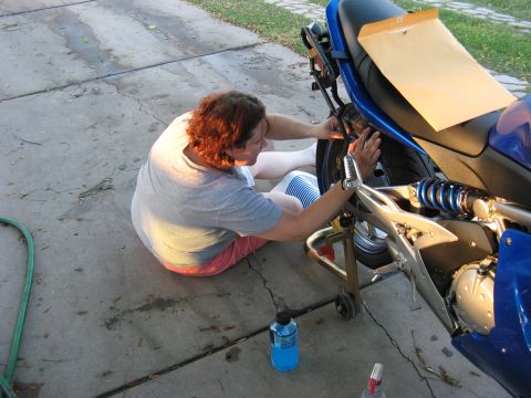 2007 Kawasaki Ninja - A person works on the rear wheel and suspension of a blue motorcycle that is elevated on a stand.