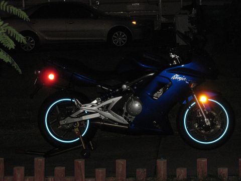 2007 Kawasaki Ninja - A blue motorcycle with reflective rim stripes is parked at night, with "Ninja" visible on its side.