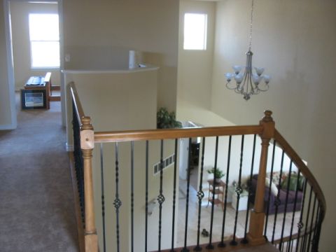 1995 Ford Bronco - A view from a landing shows a staircase with a wooden banister and black spindles, leading down to a living area with a chandelier overhead.