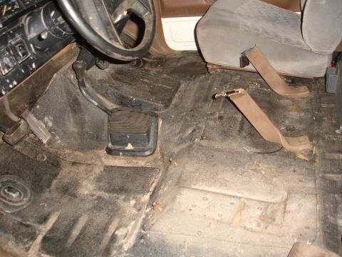 1989 Ford Bronco - The interior floor of a vehicle shows dirt, grime, and seatbelt anchor points.