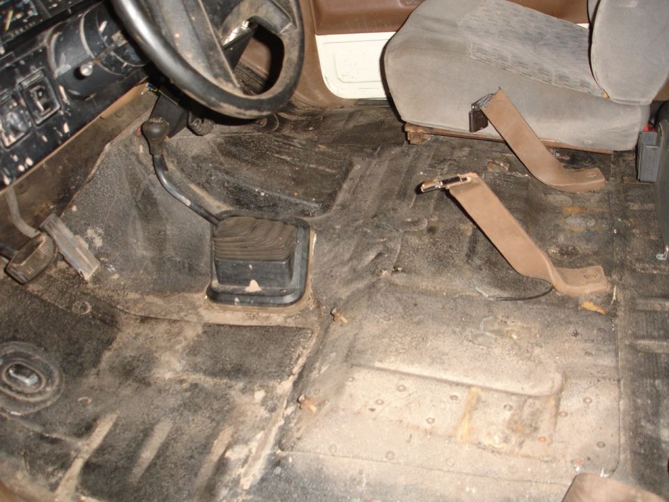 Driver's side floor and pedals of a vehicle, with seatbelt anchors visible on the floor