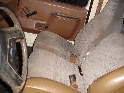 1989 Ford Bronco - Interior view of a vehicle's front seats and door panel, showing the seat fabric and seatbelt buckles.