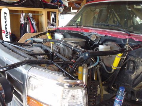 1984 Ford Bronco - Close-up of a truck's engine bay, showing modifications like a roll cage and aftermarket suspension components.