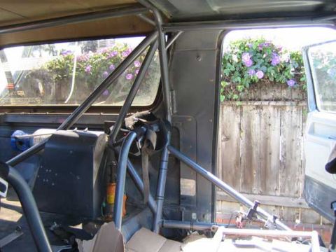 1984 Ford Bronco - The interior of a vehicle is visible, a prominent roll cage and a racing seat.