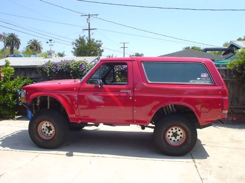 1984 Ford Bronco - This red SUV is modified with off-road suspension and large tires, suggesting it's built for terrain.
