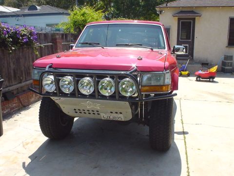 1984 Ford Bronco - This red Ford Bronco features a custom front bumper with multiple lights and a skid plate.