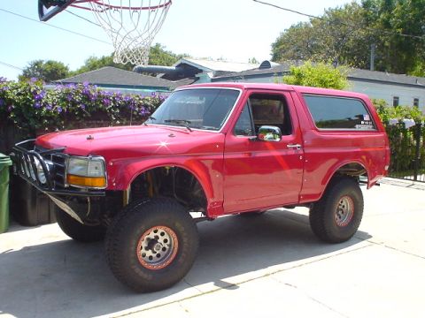 1984 Ford Bronco - This red Ford Bronco features off-road modifications and is parked in a driveway.