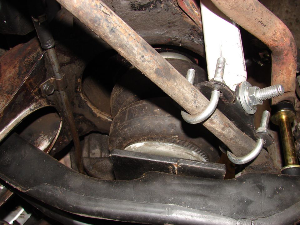 Underbody air spring bag held by U-bolt and studs among rusty suspension parts