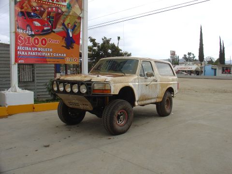 1984 Ford Bronco - This modified Ford Bronco is parked in front of a billboard advertising a promotion.