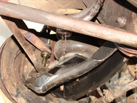 1973 Ford Ranchero - Close-up underside view of a vehicle's front suspension showing a rusty upper control arm, a coil spring, and a large black rubber componen…