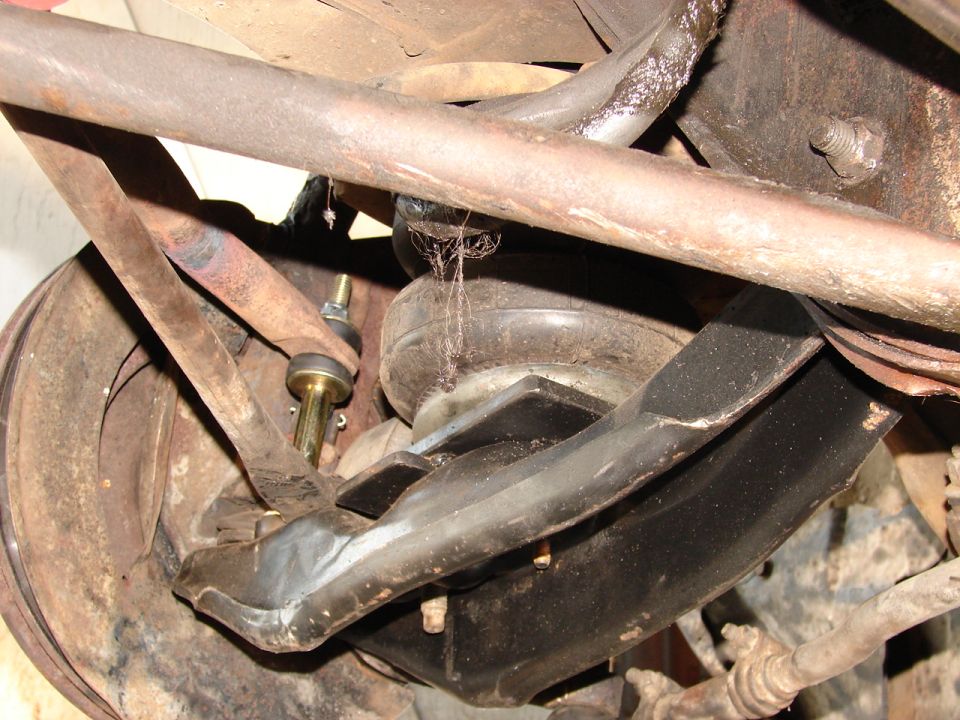 Underside suspension components with rusty control arm, coil spring, and gold bolt