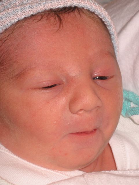 1990 Ford Bronco - Close-up portrait of a newborn baby's face wearing a pink and blue striped hospital knit cap, wrapped in a white blanket.