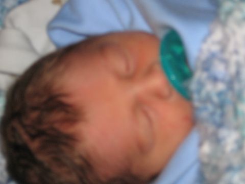 1990 Ford Bronco - Close-up of a sleeping newborn with dark hair, wrapped in a light blue blanket beside a green pacifier and a blue-and-white patterned quilt…