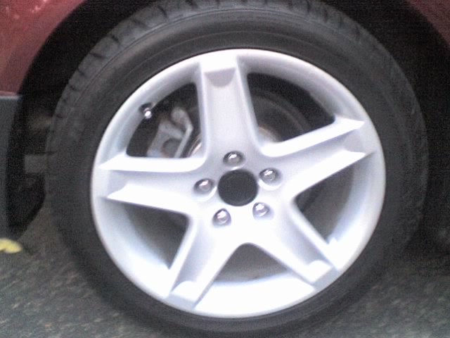 Red vehicle's silver five-spoke wheel and tire, showing brake caliper