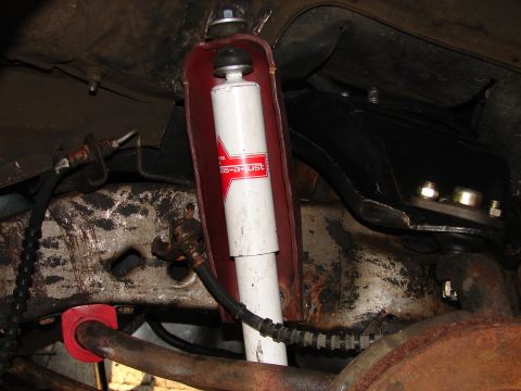 1973 Ford Ranchero - Underside view of a newly installed white KYB Gas-a-just shock absorber mounted inside a red-painted bracket, surrounded by grimy suspensio…
