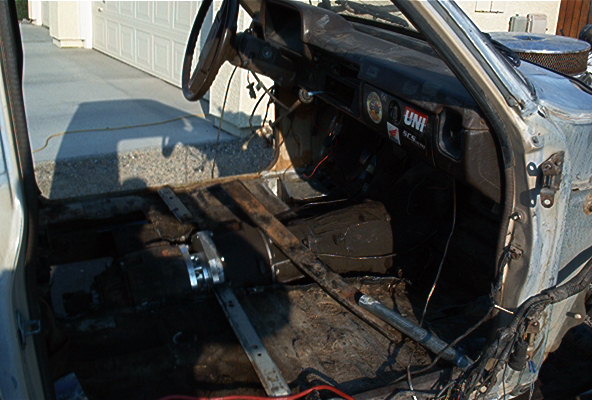 Gutted truck interior with seats and floor removed exposing transmission and wiring