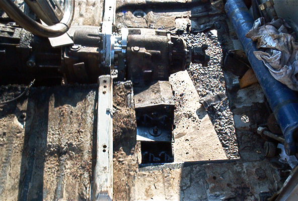 close-up of vehicle's transmission and transfer case, with surrounding frame and gravel