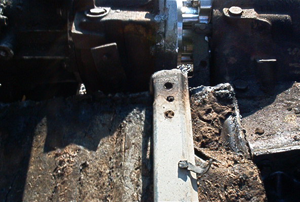 Bare-steel drilled bracket welded to a greasy truck frame rail near the transmission