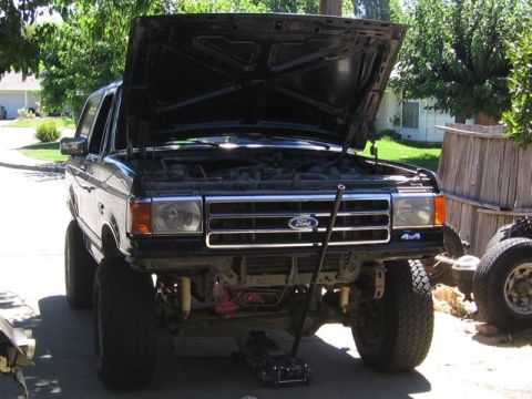 1989 Ford Bronco - 1989 Ford Bronco front view, hood up, undergoing maintenance with a floor jack.